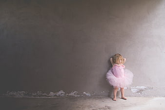 Little girl in pink tutu standing against gray wall