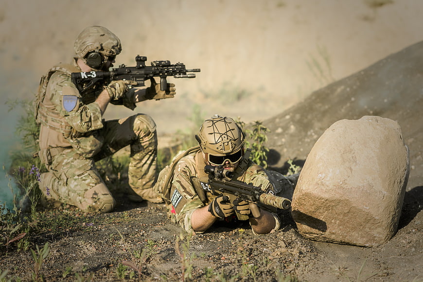 Two soldiers in tactical gear aiming rifles in a desert environment