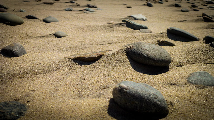 Smooth stones scattered on sandy beach texture