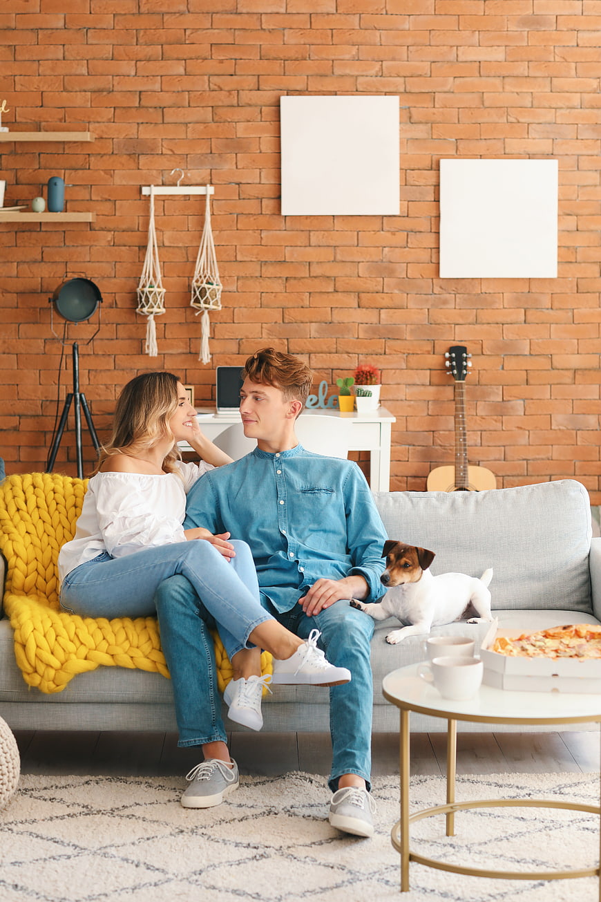 Happy couple relaxing on sofa with dog and pizza