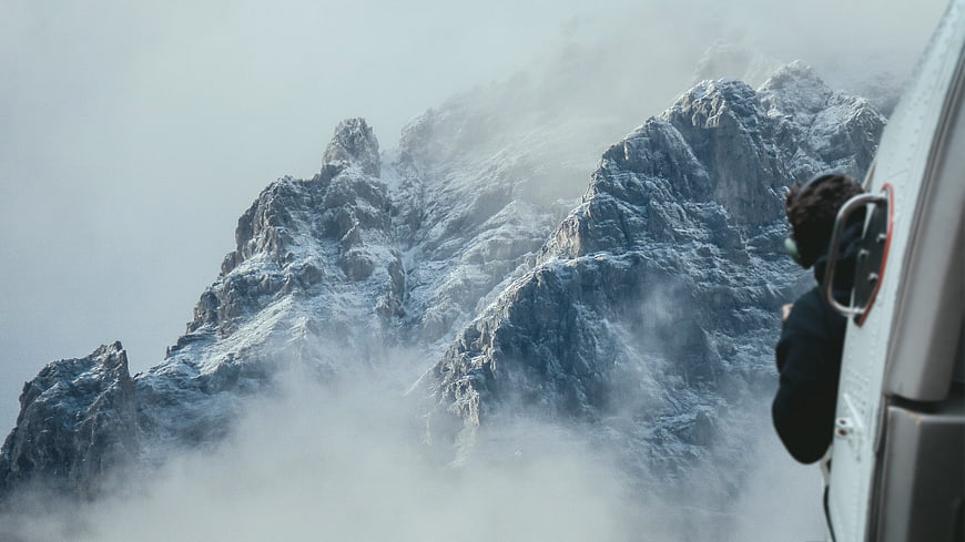 Helicopter Pilot Viewing Snowy Mountain Peaks Through Fog
