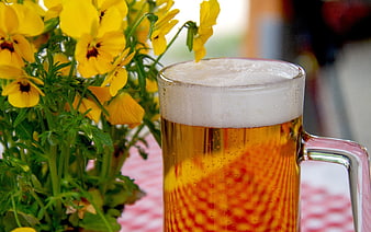 Cold beer mug with yellow pansies on checkered tablecloth