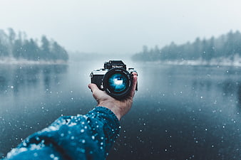 Hand holding vintage Nikon camera in snowy winter landscape