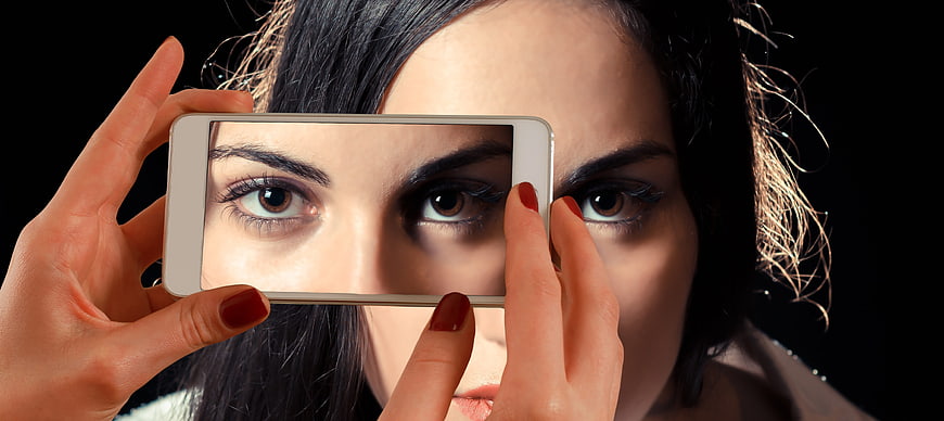 Woman holding smartphone over eyes creating double vision effect
