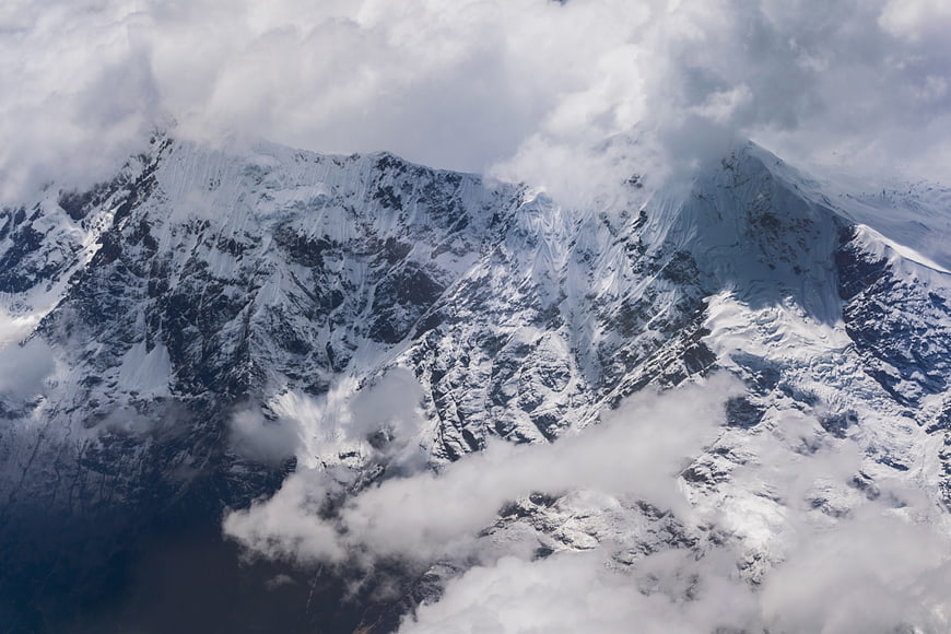Aerial View of Snow-Covered Mountain Peaks Through Clouds