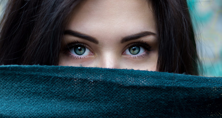 Close-up portrait of woman with green eyes peeking over teal fabric