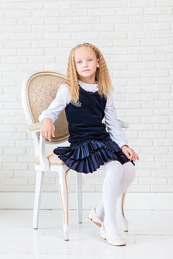 Cute little girl in navy dress sitting on vintage chair