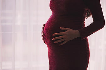 Pregnant woman in red dress holding belly by window