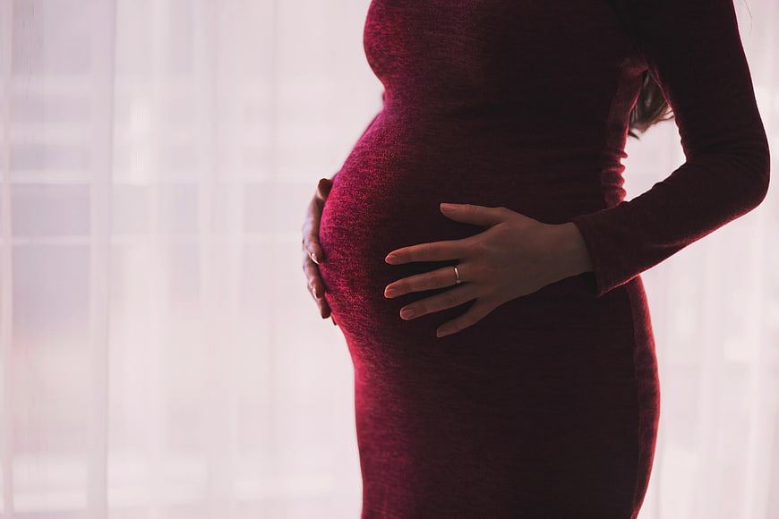 Pregnant woman in red dress holding belly by window