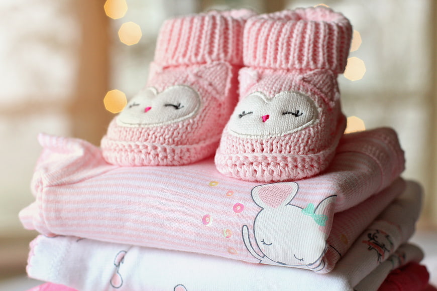 Cute pink knitted baby booties on folded clothes