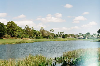 Serene golf course lake with lush green fairways and blue sky