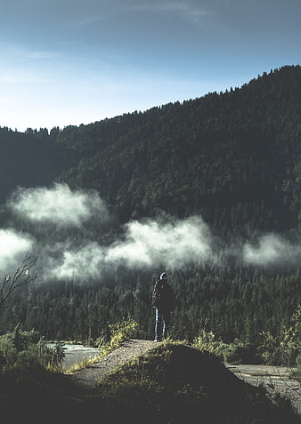 Lone hiker standing on ridge overlooking misty mountain forest