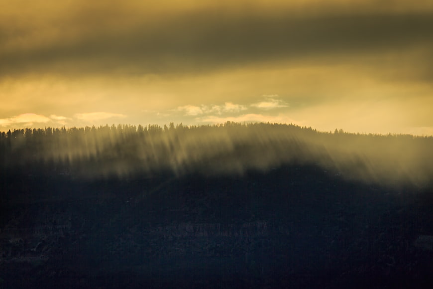 Dramatic Sunbeams Over Misty Forested Mountain Ridge