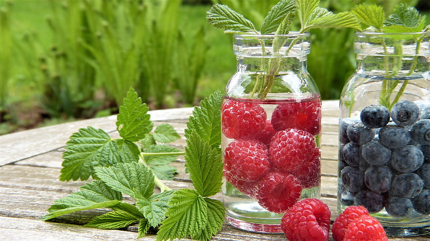 Fresh Raspberries and Blueberries in Glass Bottles on Wooden Table