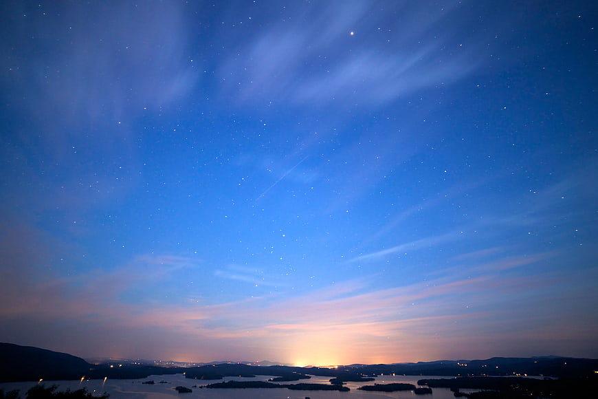 Starry Night Sky Over Lake and Distant City Lights