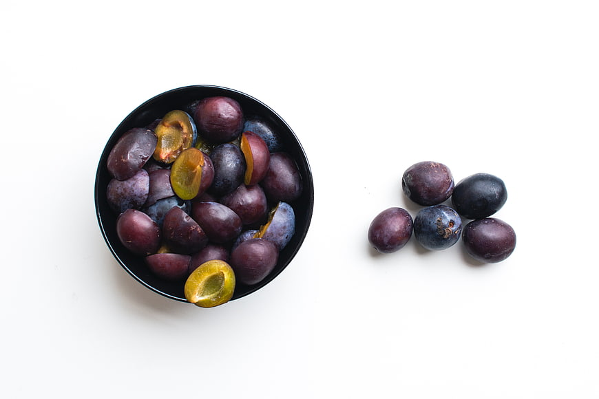 Top view of fresh plums in a black bowl on white background