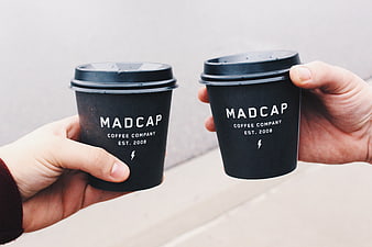 Two Hands Holding Black Coffee Cups with White Text