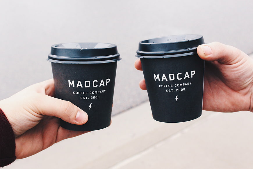 Two Hands Holding Black Coffee Cups with White Text