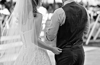 Black and white photo of bride and groom holding hands from behind