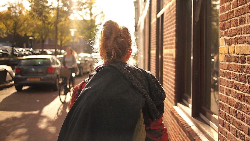 Woman Walking on Sunny Street with Brick Building