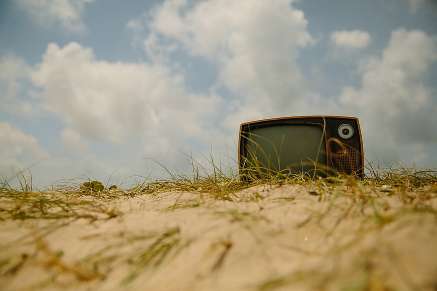 Vintage Television Set in Sandy Grass Under Blue Sky