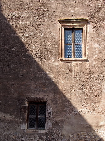 Old textured wall with two windows and diagonal shadow