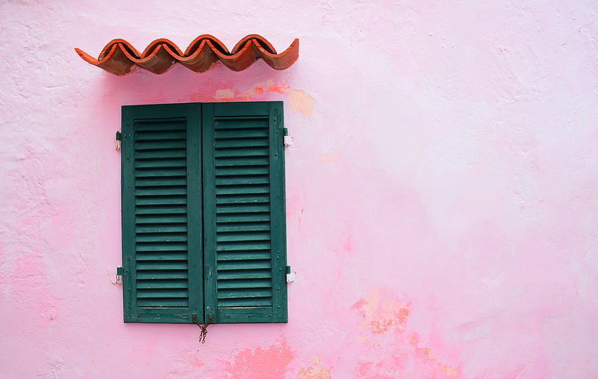 Green shutters on a pink wall with terracotta roof tiles