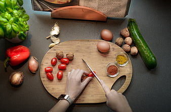 Top view of hands chopping tomatoes on wooden board with fresh vegetables
