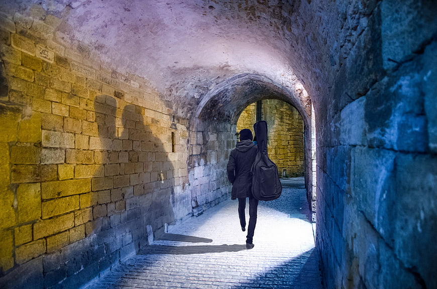 Man with Guitar Case Walking Through Stone Tunnel