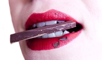 Close-up of woman's red lips biting dark chocolate bar