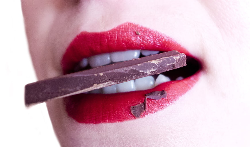 Close-up of woman's red lips biting dark chocolate bar