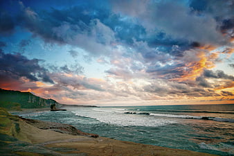 Dramatic Sunset Over Rocky Coastline with Cloudy Sky