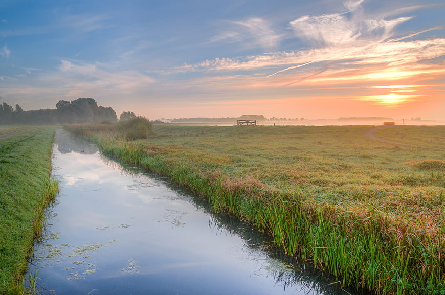 Serene rural landscape with canal at sunrise and misty fields