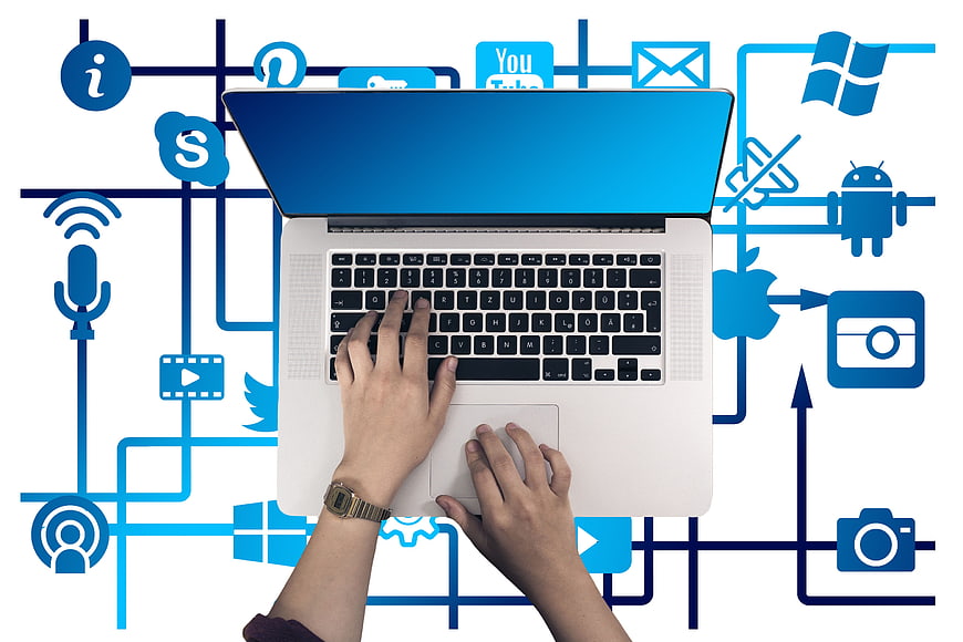 Top view of hands typing on laptop with social media icons