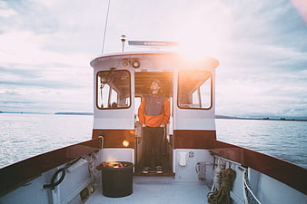 Man standing on boat deck looking up at sunset