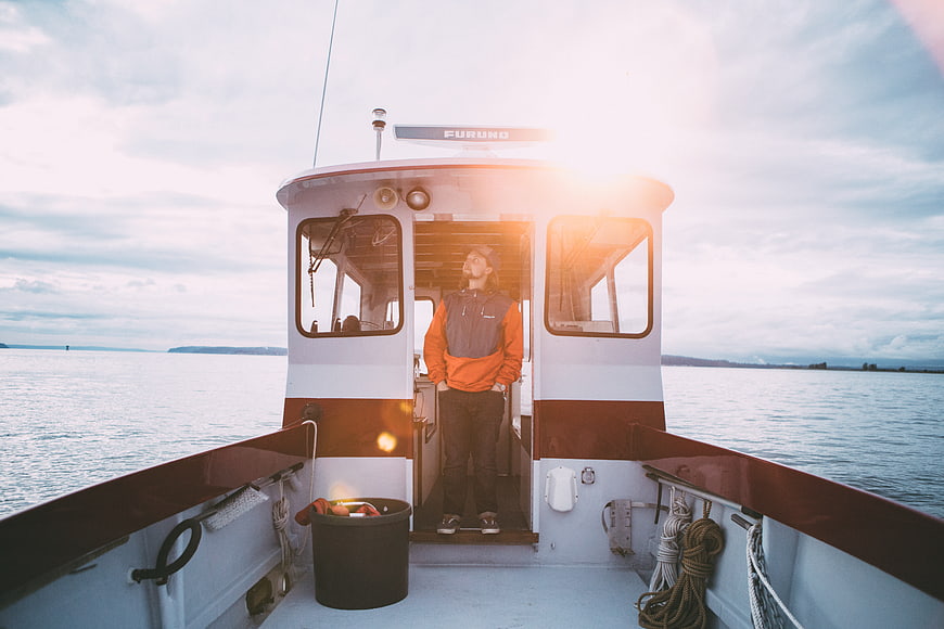 Man standing on boat deck looking up at sunset