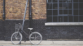 Black bicycle with basket leaning against brick wall