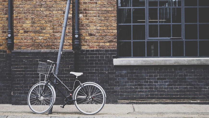 Black bicycle with basket leaning against brick wall