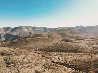 Arid mountain landscape with dry riverbed and blue sky