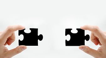 Two Hands Holding Black Puzzle Pieces Against White Background