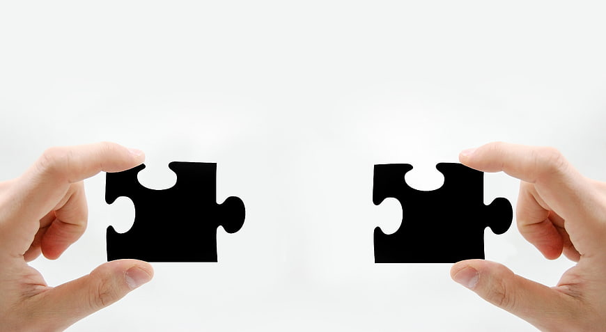Two Hands Holding Black Puzzle Pieces Against White Background