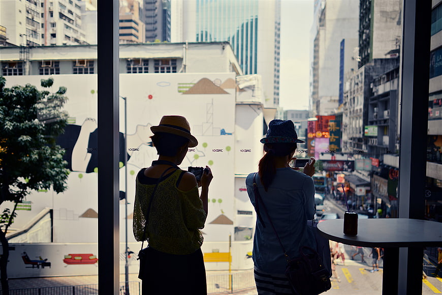 Two women taking photos of Hong Kong street view from cafe window