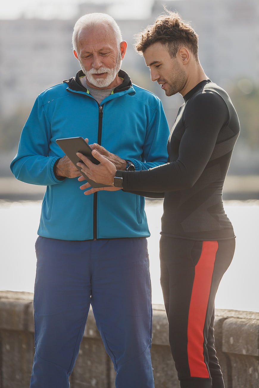 Senior and Young Man Checking Fitness Tablet Outdoors