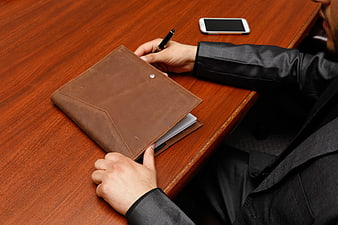 Businessman Writing in Leather Notebook at Wooden Desk