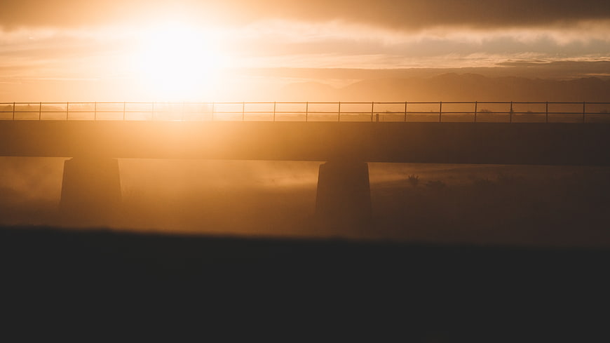 Silhouette of bridge at sunrise with foggy landscape