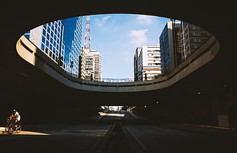 Cyclist riding through urban underpass with city skyline view