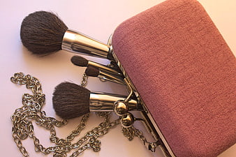 Vintage makeup brushes and pink clutch bag on white background