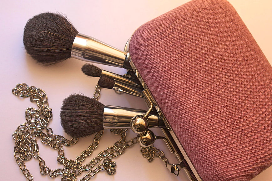 Vintage makeup brushes and pink clutch bag on white background