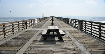 Empty wooden pier with picnic tables extending over the ocean