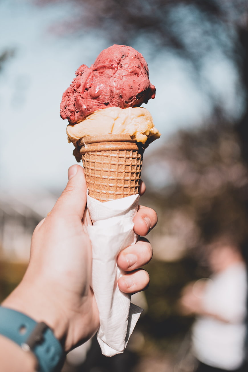Hand holding two-scoop ice cream cone outdoors